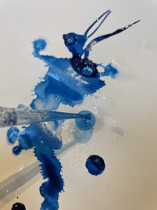 Weißes Blatt auf das mit einer Pipette blaue Tusche hinaufgetropft wird.