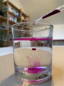 Wasserglas in das ein Tropfen pinke Tusche hineingetraut worden ist in einem Kunsttherapie Atelier