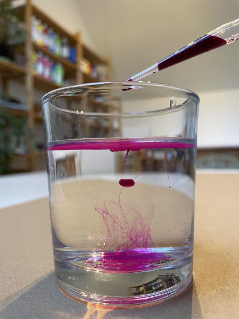 Wasserglas in das ein Tropfen pinke Tusche hineingetraut worden ist in einem Kunsttherapie Atelier